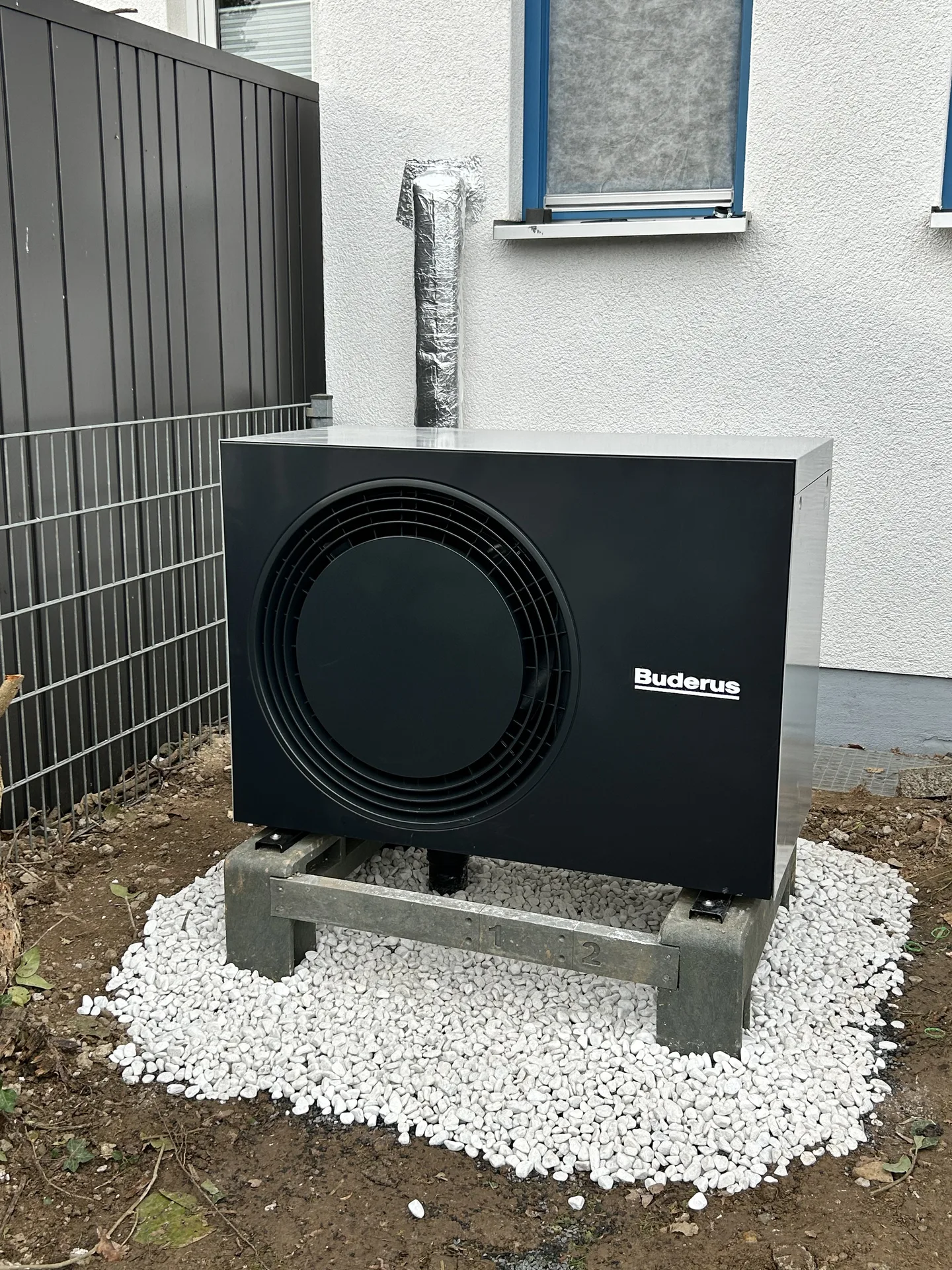 Buderus-Wärmepumpe auf Kiesbett neben der Hauswand, Außeneinheit von vorne