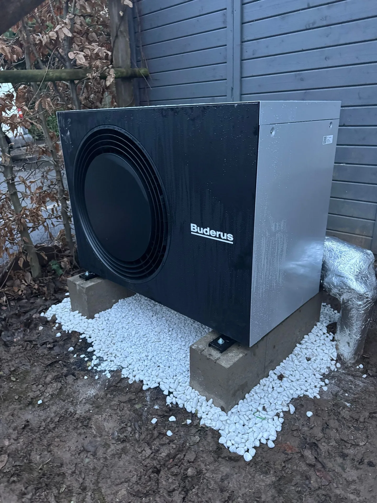 Buderus-Wärmepumpe als Außeneinheit auf Kiesbett vor einer blauen Holzwand